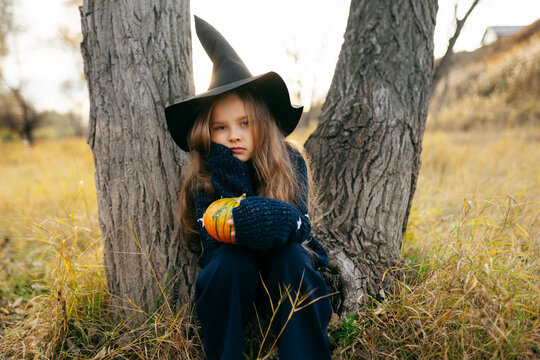 Angry girl dressed as witch and sitting near tree