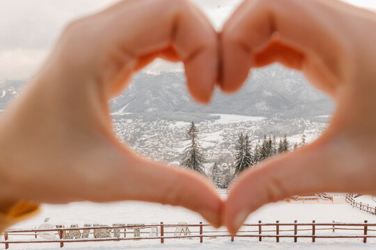 Hands of woman gesturing heart shape in front of mountains in winter