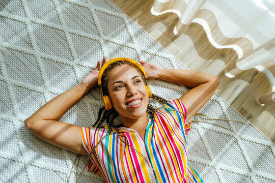 Smiling woman wearing wireless headphones and listening to music on carpet
