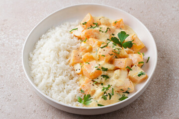 Bowl of pumpkin in sour cream sauce with rice sprinkled with fresh parsley on beige textured stone table, top view. Vegetarian food
