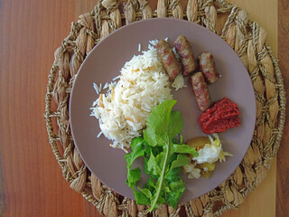 Meatballs, rice, pickles, sauce and arugula leaves served on a plate.