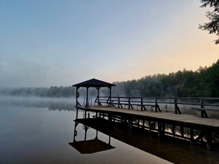 Naklejka premium A serene photograph of a wooden dock at calm, mist-covered lake at dawn