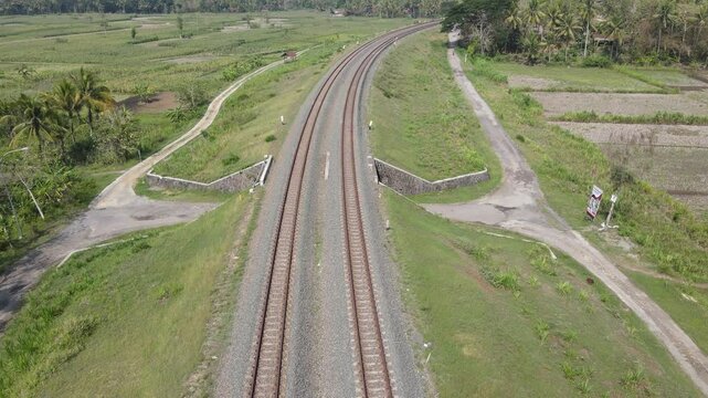 drone shot, double track railway with left and right rural rice fields. There is a tunnel for land vehicle passage.
