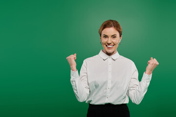 A dynamic woman in a crisp white shirt exudes confidence and joy with a victorious pose in a professional space.