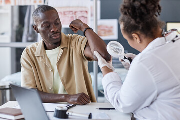 Portrait of adult African American man visiting dermatologist with female doctor examining skin...
