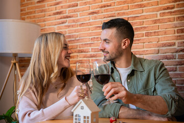 A joyful couple toasts with red wine, smiling and enjoying a warm moment together in a cozy indoor setting. The image conveys celebration, connection, and relaxation in a casual atmosphere.
