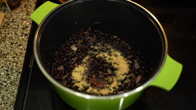 Adding spices to the vegetable stew with beans simmering on electric stove top