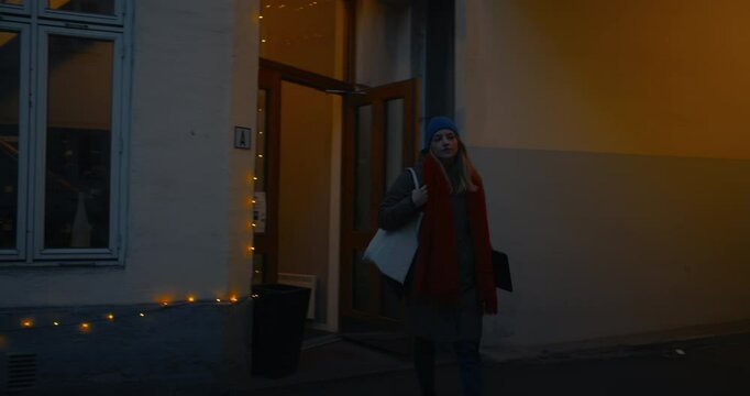 Woman walk down stairs from apartment to the indoor yard of building to bicycle parking. Load belongings to cargo electric bicycle pannier bags. Early morning commute in winter scandinavian city