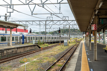 Fototapeta premium Trains stop at a quiet Japanese railway station on a cloudy day with empty platforms and a serene atmosphere