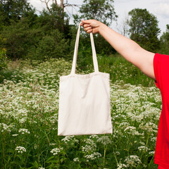 Mature woman, female hand holding white bag canvas fabric for mock up blank template on meadow with...