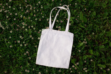 White cotton or mesh bag on green grass with clover flowers background. Zero waste, no plastic, eco...