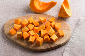 Pumpkin cut into pieces on a wooden board on a beige textured background