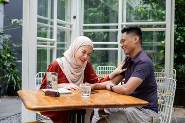 A joyful couple sharing laughter and bonding at an outdoor cafe table, surrounded by lush greenery and cozy atmosphere. Perfect representation of happiness and connection.