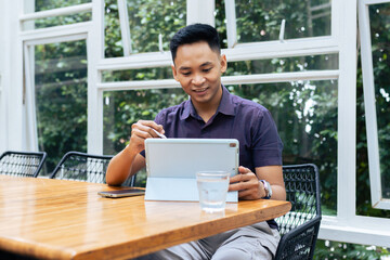 Fototapeta premium A young professional sits at a wooden table in a bright office, using a digital tablet for work.
