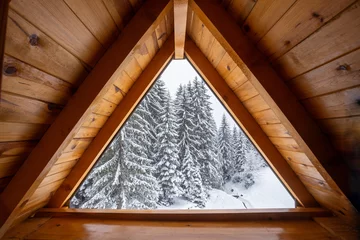 Fototapete Rund Rot Lila Cozy wooden attic window framing stunning snow covered pine forest  © MexChriss