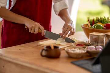 Chef cutting white onion on wooden board with sharp knife