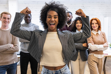 Young businesswoman flexing biceps, celebrating success with multi ethnic colleagues in coworking...