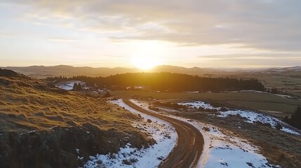 Obraz premium Winding Road Through Snowy Hills and a Forest at Sunset