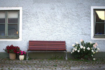 Wooden red bench against and old house with flowers and flower pots in a picturesque town.