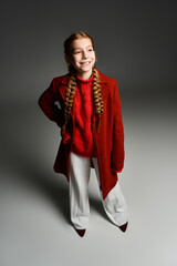 A young girl dressed warmly in a bright red sweater and stylish coat smiles happily indoors.