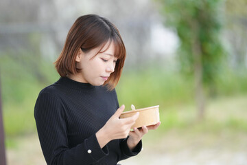 A young woman in her 20s with short hair wearing a black knitted long-sleeved shirt is sitting in a pavilion in an empty park and eating fruits such as dragon fruit, pineapple, and strawberries.