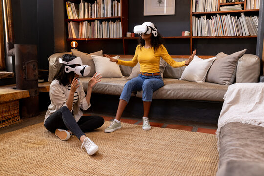 multiracial female friends using VR headsets at home, exploring virtual reality together