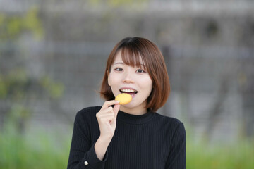 A young woman in her 20s with short hair wearing a black knitted long-sleeved shirt is sitting in a...