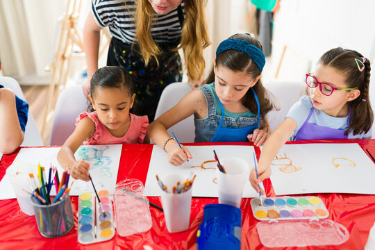 Group of elementary school students painting with watercolors and having fun during a creative art class with their teacher
