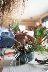 Detail of hands decorating ikebana, Japanese floral decoration workshop, in the out-of-focus background more plants.