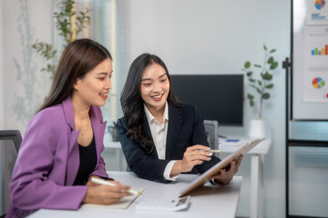 Two women in business suits are sitting at a desk looking at a presentation