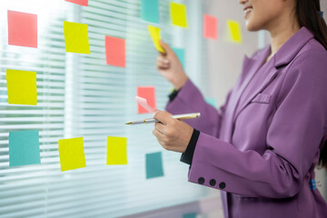 A woman in a purple jacket is writing on a board with colorful sticky notes