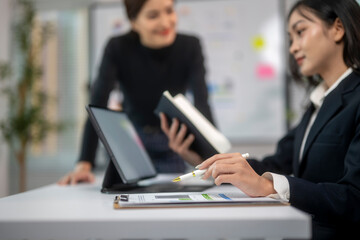 Two women are sitting at a desk with a white board behind them