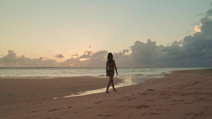 Young woman is enjoying a peaceful evening stroll on a beautiful beach in the maldives as the sun sets over the indian ocean