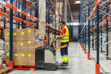 Interior of storage warehouse, Worker with electric forklift pallet jack unloading pallet goods