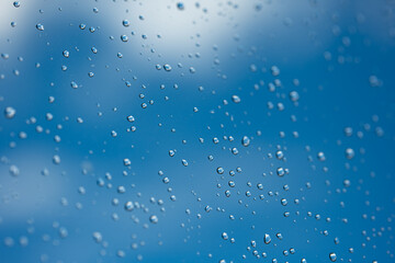 Water droplets on glass window. Blue sky and white clouds in the background, close up macro shot