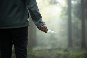 Unrecognizable Caucasian male holding a hunting knife in a foggy forest scene. Danger of traveling...