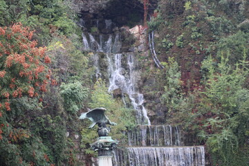 A serene waterfall cascades down rocky cliffs surrounded by lush greenery in a tranquil outdoor...