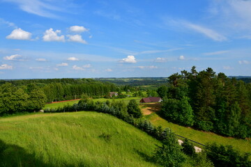 A view from the top of a tall hill or mountain showing various fields, meadows, and pasturelands surrounded with forests, moors, small villages and farmlands spotted on a sunny summer day in Poland