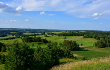 Obraz premium A view from the top of a tall hill or mountain showing various fields, meadows, and pasturelands surrounded with forests, moors, small villages and farmlands spotted on a sunny summer day in Poland