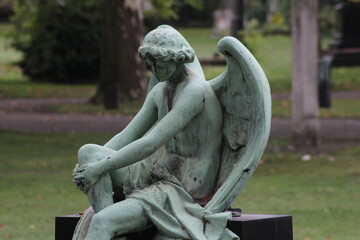 Elegant angel sculpture seated in a tranquil park, surrounded by lush greenery and serene...
