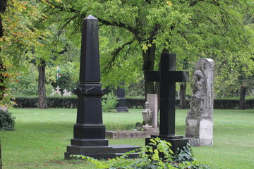 Mausoleums and gravestones surrounded by green trees in a peaceful cemetery on a calm afternoon
