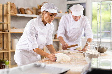 Elderly man and woman knead and roll out dough