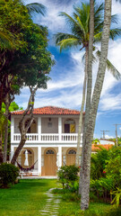 Fototapeta premium ITAPARICA, BAHIA STATE, BRAZIL: front view of luxury villa, portuguese colonial style, beautiful tropical lawn, palm trees, white walls, terracotta roof tiles, veranda and swimming pool