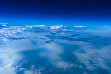 Aerial view from airplane window above green ground. View from the airplane window with beautiful clouds at sunrise. Earth and sky as seen through window of an airplane.