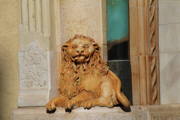 A detailed stone lion sculpture resting at the entrance of an ornate building in the late afternoon...