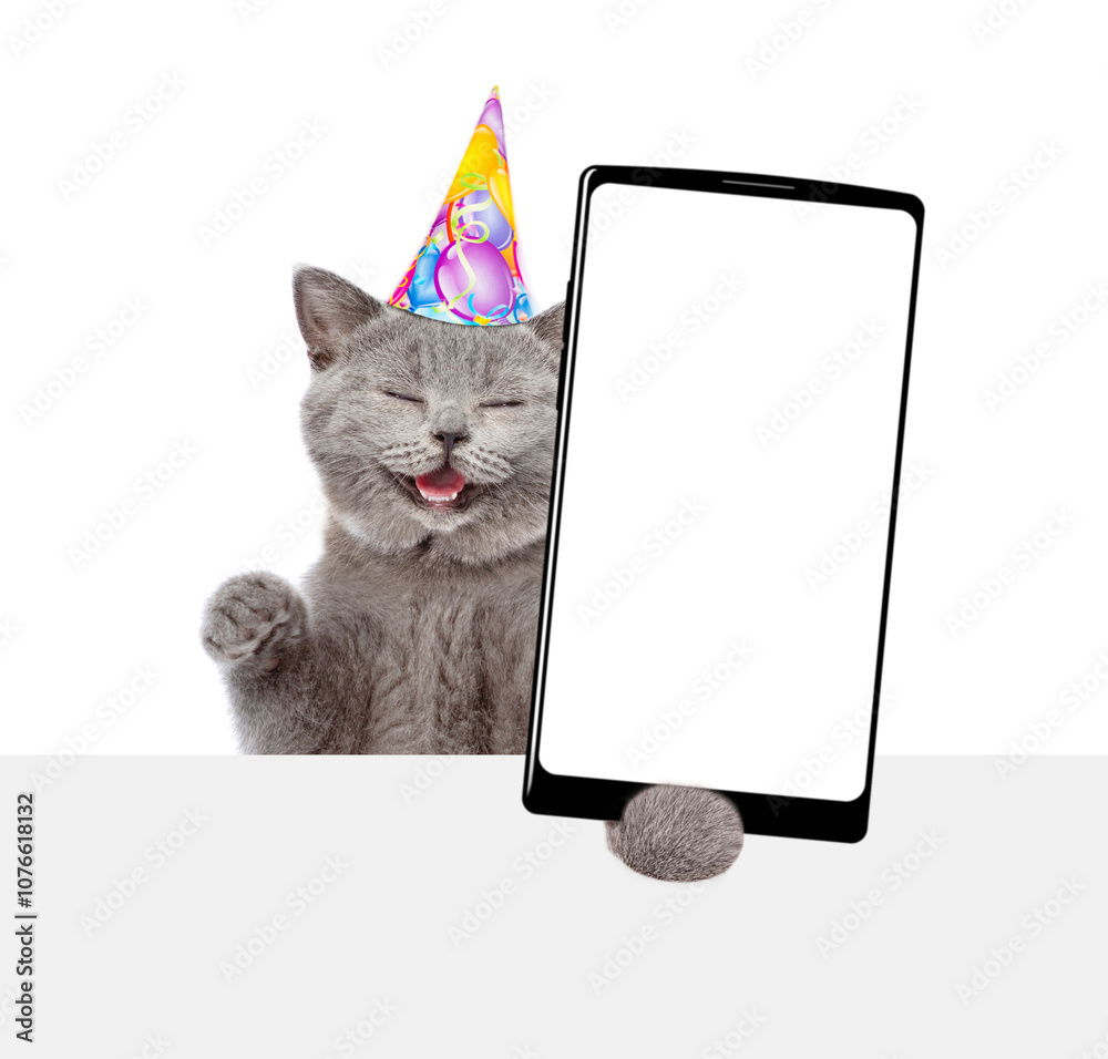 Fototapete happy cat wearing party cap shows big smartphone with blank screen above empty white banner. empty s