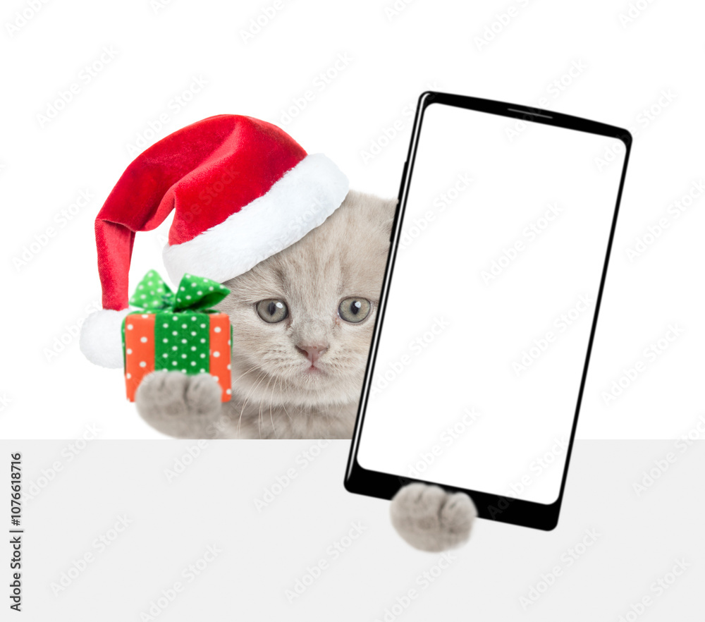 Poster cute kitten wearing red christmas hat holds tiny gift box and smartphone with white blank screen in 