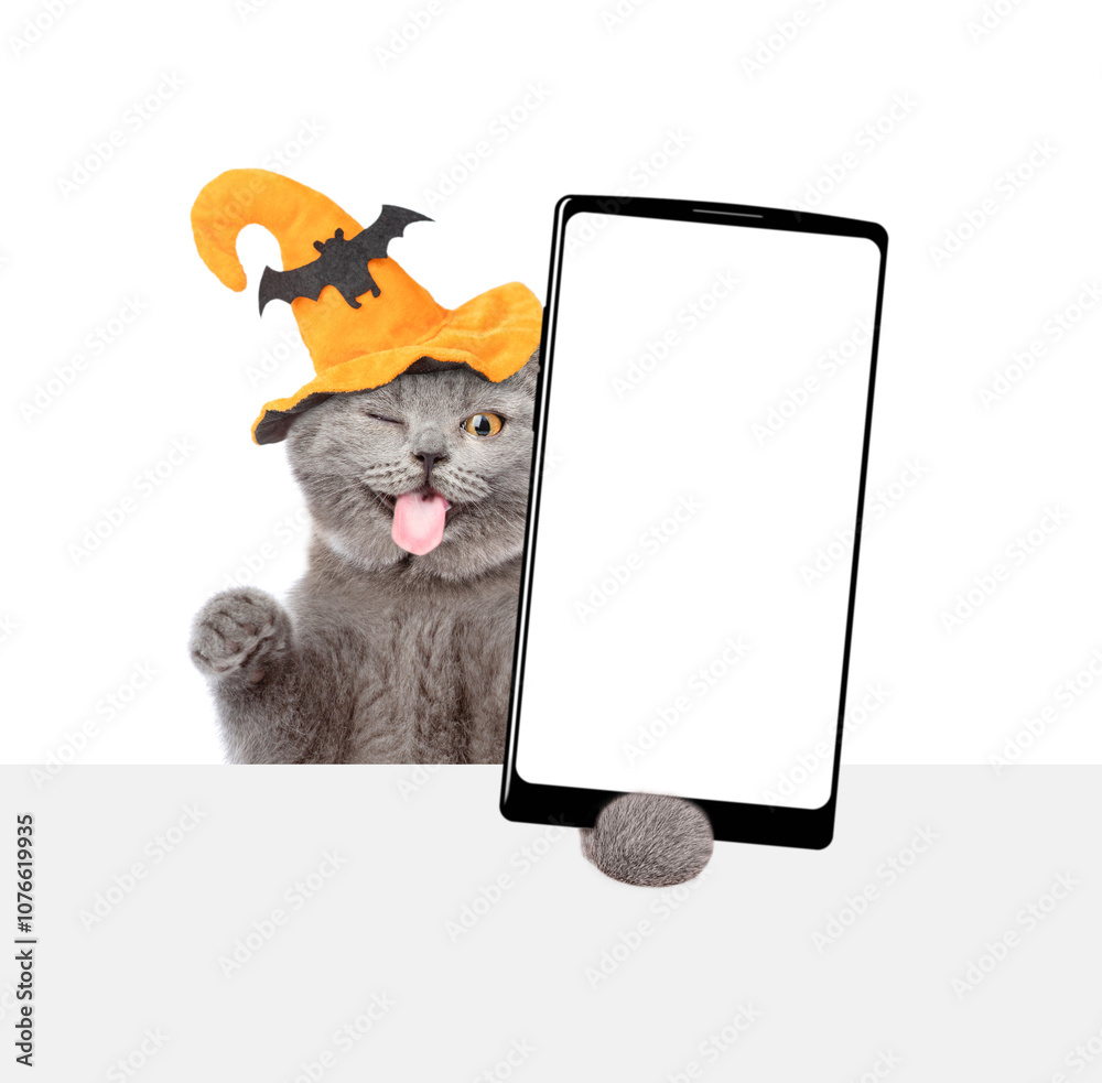 Poster winking licking lips kitten wearing hat for halloween holds shows smartphone with white blank screen