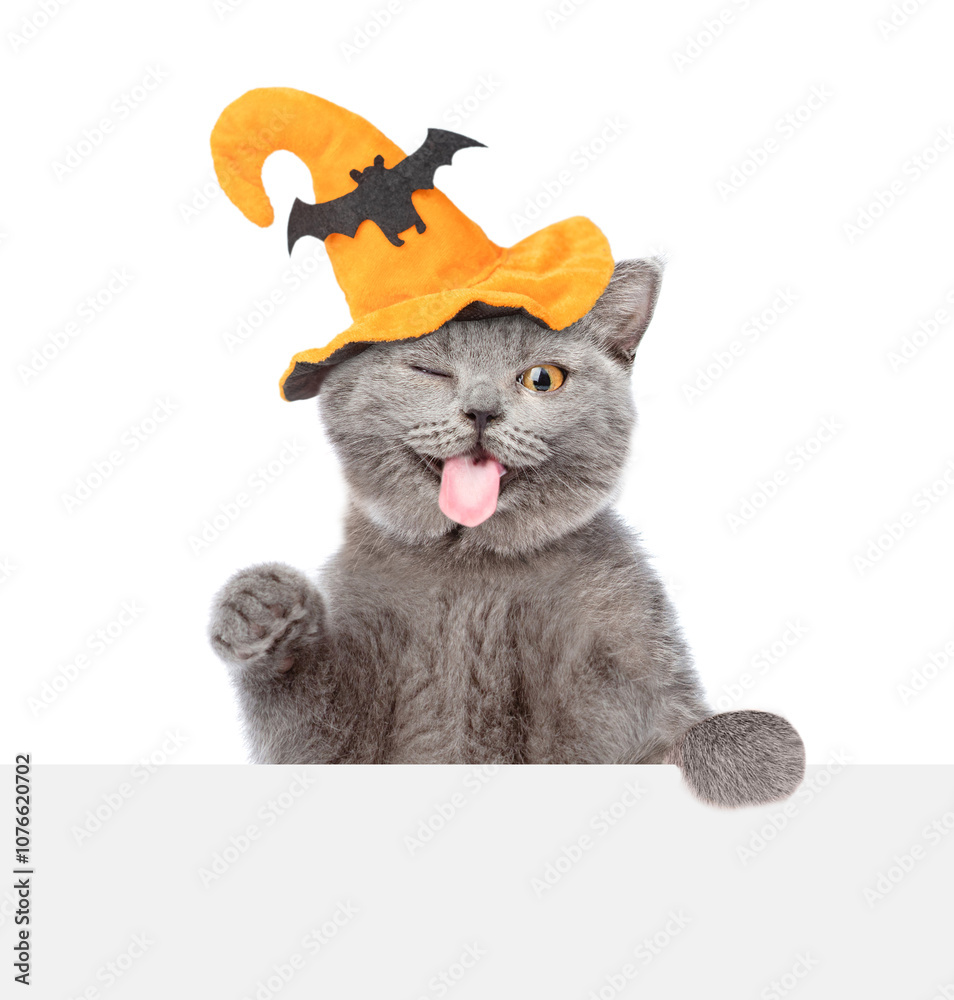 Aufkleber winking kitten with hat for halloween looks above empty white banner and sticks out tongue. isolated