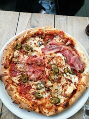 Deliciously topped personal pizza with ham, jalapeños, and chicken on a wooden table at a casual dining spot during lunchtime